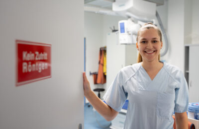 Eine junge Frau im Kasack schließt die Tür in der Radiologie, auf der 