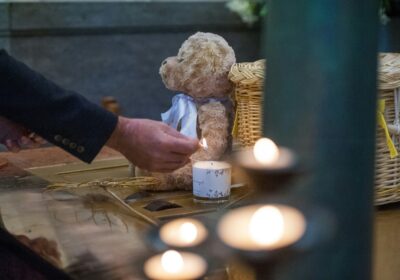 Eine Hand zündet eine Kerze an, die neben einem Teddy und einem Korb steht.