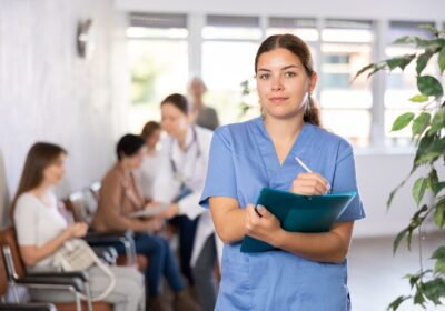 Eine gelesene Frau steht im blauen Kasack in einem Krankenhausflur.