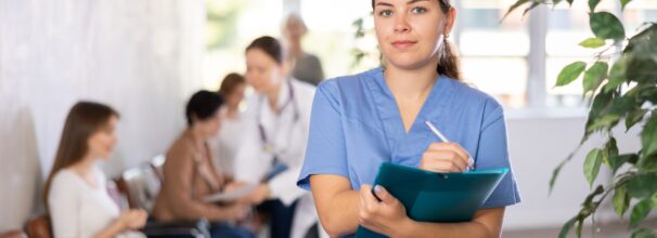 Eine gelesene Frau steht im blauen Kasack in einem Krankenhausflur.